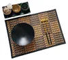 A table setting with a bamboo placemat, a black bowl, chopsticks, and small dishes with tea bags and spices. Produktbild-Vorschau