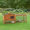 A wooden rabbit hutch with an attached run is set up on a green lawn in a garden setting. Several rabbits are visible inside the hutch and run. Náhled obrázku produktu
