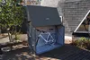 A white bicycle is stored inside a dark gray metal storage box on a wooden deck next to a house. Náhľad obrázku produktu