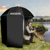 A man is fishing next to a black fishing tent by a lake. Anteprima dell’immagine prodotto