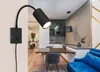 A modern interior scene featuring a black wall lamp, a dining table with chairs, a kitchen area, and a blue sofa. Produktbild-Vorschau