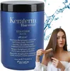 A large blue tub of hair mask is shown next to a young woman with long brown hair who is combing her hair. Water splashes are visible in the background. Podgląd zdjęcia produktu