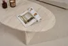 A travertine coffee table with a magazine and two decorative items on it, placed on a textured rug. Anteprima dell’immagine prodotto