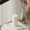 A white LED candle with a lit flame sits on top of a stack of books, next to a glass vase with red berries. Podgląd zdjęcia produktu