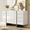 A modern white sideboard with a high-gloss finish, featuring two doors and four drawers, is displayed in a well-lit room with decorative items on top. Anteprima dell’immagine prodotto