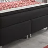 A close-up view of a black box spring bed with a red and white patterned duvet. Produktbild-Vorschau