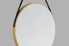 A round mirror with a gold frame and a black leather-look strap hanging against a plain gray background. Náhled obrázku produktu