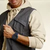A man wearing a vest and hoodie, showing off his watch. Produktbild-Vorschau