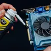 A hand is holding a can of K2 isopropyl alcohol and spraying it onto a computer graphics card. Podgląd zdjęcia produktu