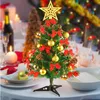 A decorated mini Christmas tree on a table setting with other blurred Christmas decorations in the background. Produktbild-Vorschau