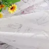 A close-up of white sheer curtains with a floral and text pattern, with yellow flowers in the upper left corner. Produktbild-Vorschau