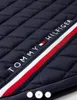 A close-up of a quilted navy blue saddle pad with a red, white, and blue stripe and the Tommy Hilfiger logo. Produktbild-Vorschau