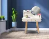 A white vanity table with a round mirror and wooden legs, set against a blue wall with a large potted plant and a radiator. Produktbild-Vorschau