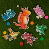 Several dragon puzzle pieces and colorful game pieces are scattered on a green, grassy surface. Produktbild-Vorschau
