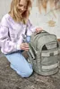 A young girl is kneeling and placing a water bottle into a backpack. Produktbild-Vorschau