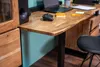A close-up view of a wooden desk with a live edge, featuring a laptop, a game controller, and a drawer unit. Produktbild-Vorschau