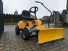 A yellow snow plow attachment for a riding lawn mower is parked on a paved driveway. Produktbild-Vorschau