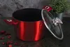 A red pot with a glass lid is displayed on a dark surface, with dried rose petals scattered around and a potted plant in the background. Voir les images du produit