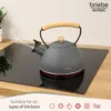 A gray kettle with a wooden handle is steaming on a black induction stovetop. Náhľad obrázku produktu