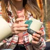 Frau hält die "Climbing Mug Evo Keramiktasse mit Klettergriff" von YY Vertical im Freien. Podgląd zdjęcia produktu