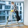 A woman is cleaning a large window while standing on a foldable ladder. Anteprima dell’immagine prodotto