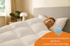 A woman sleeping comfortably under a thick white duvet in a bedroom. Produktbild-Vorschau