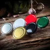 A collection of colorful jar lids arranged on a rustic wooden surface, with garlic and a jar in the background. Podgląd zdjęcia produktu