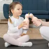 A young girl is sitting on a mat, holding a unicorn-shaped water bottle while another hand offers her another one. Anteprima dell’immagine prodotto