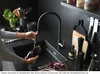 A person is washing an eggplant under a black kitchen faucet in a modern black kitchen. Podgląd zdjęcia produktu