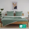 A neatly made bed with green bedding and pillows, set against a white wall with a framed abstract artwork. Voir les images du produit