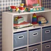 A white shelving unit filled with children's toys and storage boxes, set against a blue and white checkered wallpaper. Produktbild-Vorschau