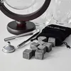 A set of whiskey stones, tongs, and a funnel are arranged on a white surface, with a globe-shaped decanter and glasses in the background. Náhľad obrázku produktu