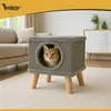 A cat is sitting inside a modern cat house with wooden legs, placed on a carpet in a living room setting. Produktbild-Vorschau