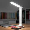 A white LED desk lamp with a wireless charging pad is shown on a wooden desk, with a laptop and bookshelves in the background. Produktbild-Vorschau