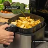 A hand is shown operating an air fryer filled with french fries. Vegetables are visible in the background. Produktbild-Vorschau