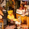 A miniature bistro scene with a teddy bear, food, and drinks. Voir les images du produit