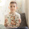 A young boy is holding a round wall clock with a cat illustration in a room. Produktbild-Vorschau