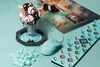 A light blue gaming mouse and keyboard keys are arranged around a sundae with chocolate syrup and a waffle cone, with a bottle and a picture in the background. Produktbild-Vorschau