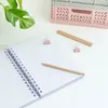 A flat lay of a notebook, pencils, and binder clips on a white surface, with a plant in the background. Náhľad obrázku produktu