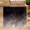 A top-down view of two black cutting boards with a marble-like pattern, placed on a wooden surface. Other kitchen items are visible in the background. Voir les images du produit