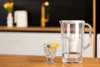 A clear plastic water filter pitcher and a glass of water with lemon and mint are on a wooden table in a kitchen. Produktbild-Vorschau