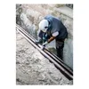 A worker is using a reciprocating saw to cut pipes in a trench. Voir les images du produit