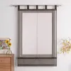 A sheer dark gray Roman blind with tie-up loops hangs on a window rod against a white wall. A wooden dresser with a framed floral picture and sunflowers is to the left, and a decorative branch with yellow leaves is to the right. Produktbild-Vorschau