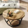 A round wooden coffee table with a black metal base, decorated with a vase of flowers and two books. Produktbild-Vorschau