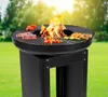 A black grill with food cooking on it, set up outdoors on a grassy lawn with trees in the background. Produktbild-Vorschau