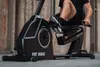 A person is using a black recumbent exercise bike outdoors. Produktbild-Vorschau