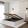 A white storage bed with its mattress support lifted, revealing the storage compartment underneath, in a bedroom setting. Produktbild-Vorschau