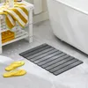 A bathroom scene with a bathtub, a shelf with towels, yellow flip-flops, and a gray bath mat. Anteprima dell’immagine prodotto