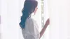 A woman is standing by a window, looking out. She is wearing a white robe and holding back a sheer curtain. Podgląd zdjęcia produktu