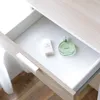A drawer opened to reveal a white textured liner with a bottle of green perfume and a small box. Produktbild-Vorschau